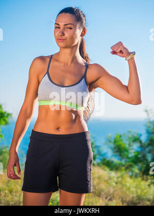 Young Active Sporty Successful Woman Standing on the high hill above sea or ocean and looking at camera. Beautiful girl in sportwear. Health concept. Stock Photo
