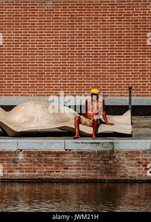 Man (60-65) tanning outside at water's edge in Milan, Italy during the height of the summer Stock Photo