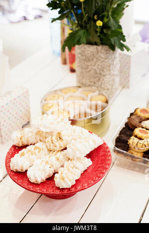 Candy bar Table with sweets, candies, dessert. French meringue cookies in red high plateau, tray. Egg white sweets, biscuits and flowers on a white wo Stock Photo