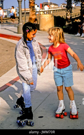 Two ethnically diverse girls 6-8-years old laughing and having fun together on roller skates in Santa Barbara, California Stock Photo