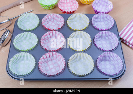 Very colourful paper cupcake liners placed in a baking tray ready to be filled on a kitcken table Stock Photo