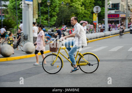 A Chinese gentleman rides a bicycle with a wicker basket on the front down a road in Shanghai, China. Stock Photo