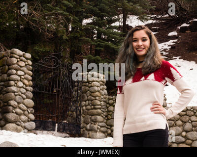 A smiling teen girl in red and white sweater by an iron gate with stone gateposts in winter Stock Photo