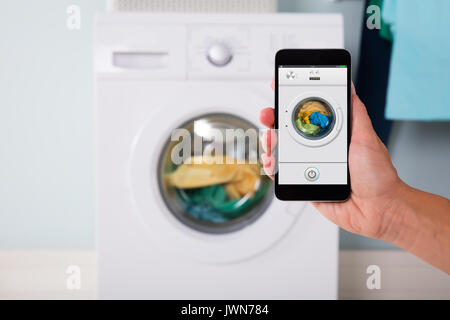 Close-up Of Person Hand Operating Smart Washing Machine Using Mobile Phone App Stock Photo