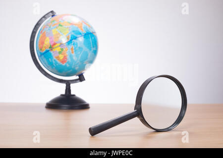 Side view of black magnifying glass and small multicolored globe on wooden surface over white background Stock Photo
