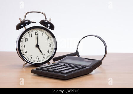 An old fashioned analogue clock, calculator and magnifying glass on an office desk with white background and copy space. Stock Photo