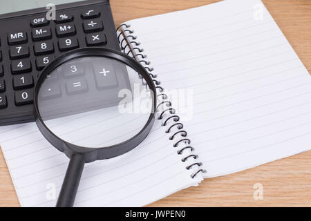 Open blank spiral binder with calculator and magnifying glass on wooden desk Stock Photo