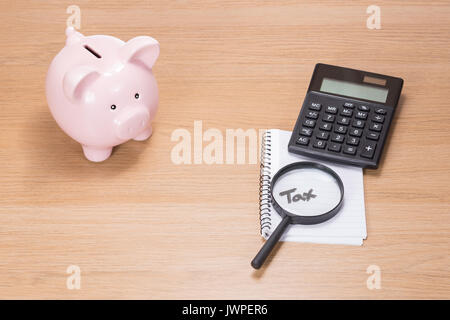 Piggy bank, calculator and magnifying glass resting on a notebook with the handwritten word - Tax - in a financial concept of paying and calculating t Stock Photo