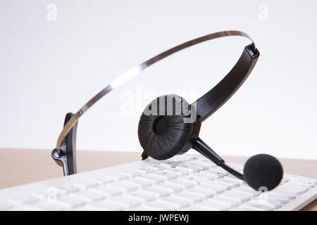 Business communication concept with a modern black headset lying on a white computer keyboard with focus to the earpiece Stock Photo