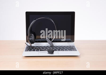 Laptop computer with a headset lying on the open keyboard on a wooden desk in a concept of business or company communications Stock Photo