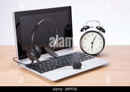 Alarm clock alongside an open laptop computer and headset on a wooden desk in a concept of business communications Stock Photo