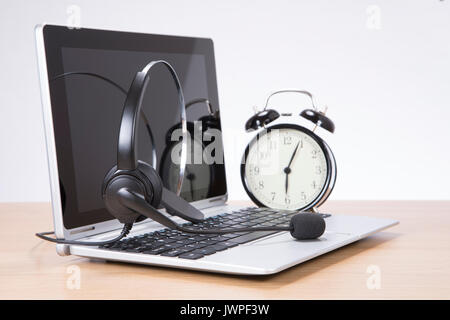 Alarm clock standing on desk by headset on laptop keyboard Stock Photo