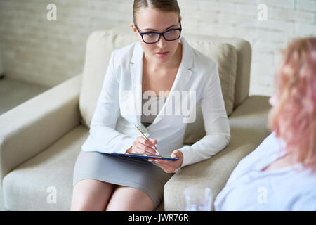 Portrait of beautiful young woman making notes while consulting patient during therapy session in office, offering psychological guidance Stock Photo