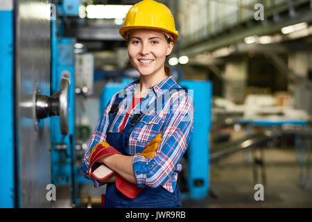 Portrait of beautiful young woman in hardhat smiling confidently at camera enjoying work in modern factory Stock Photo