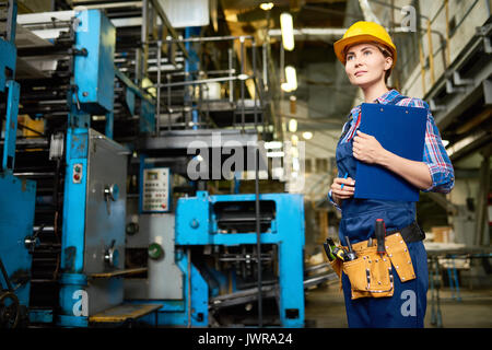 Portrait of young woman working in modern factory, walking between operating machines holding clipboard Stock Photo