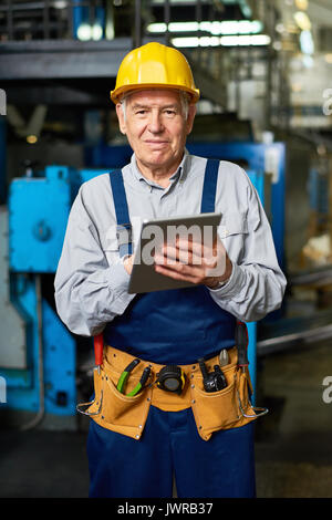 Portrait of senior factory worker using digital tablet and smiling at camera posing in modern workshop Stock Photo