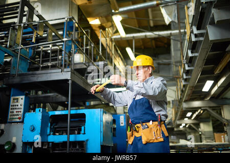 Portrait of senior mechanic checking measurements with reel tape while working in modern factory Stock Photo