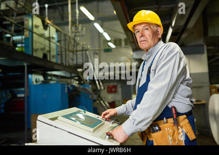 Portrait of senior man operating machine units in modern factory standing by control panel and looking away Stock Photo