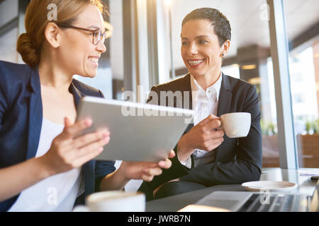Cheerful pretty coworkers chatting animatedly with each other while having coffee break in lovely small cafe with panoramic windows Stock Photo
