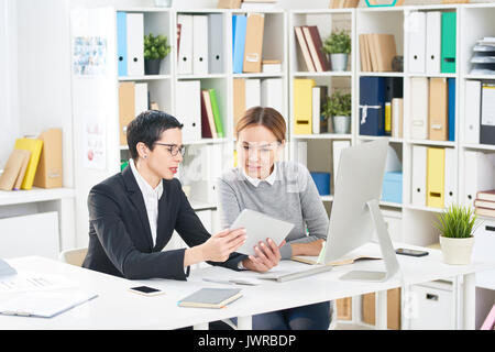 Multi-ethnic group of talented interior designers gathered together at office desk and discussing joint project, they using digital tablet Stock Photo