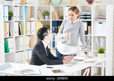 Multi-ethnic group of coworkers analyzing statistic data while having working meeting in modern office Stock Photo