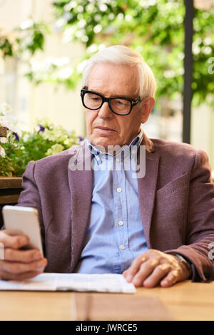Portrait of modern senior man learning to use smartphone in outdoor cafe, enjoying sunny day Stock Photo