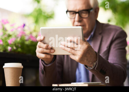 Portrait of senior man using digital tablet in outdoor cafe, focus on male hands holding modern device Stock Photo