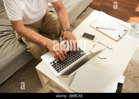 Above view of senior businessman using laptop at home, closeup of male hands typing on keyboard while working Stock Photo