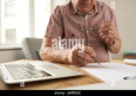 Closeup portrait of unrecognizable senior man filling in papers while working with laptop at home Stock Photo