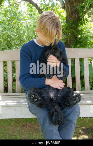 A blonde teenaged boy hugs his black dog Stock Photo