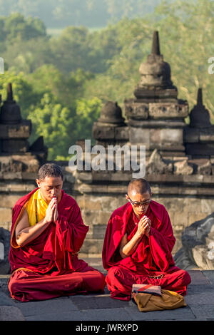 Red robed monks praying at sunrise at the world heritage site Borobudur Buddhist temple. Stock Photo