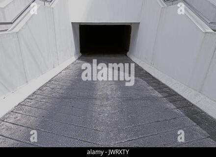 White walled underground car parking entrance to dark tunnel. Stock Photo