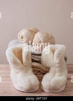 Pair of warm winter sheepskin slippers (alpaca), wool yarn  on a pile of warm woolen clothes (Selective focus) Stock Photo