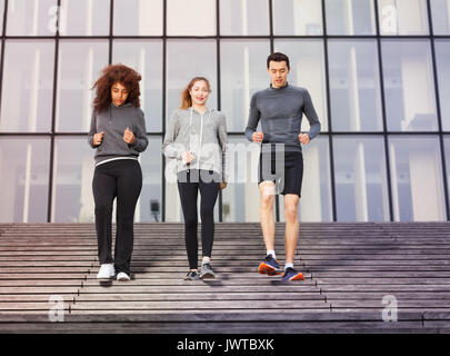 Two young women and one man going downstairs as part of their workout outdoors on city stairs Stock Photo