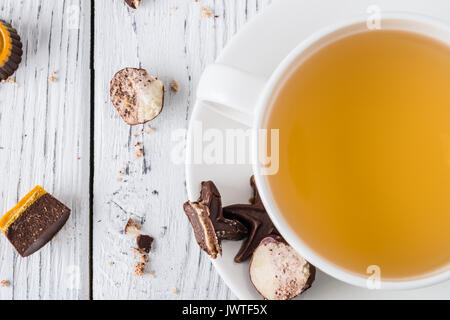 Cup of tea with raw handmade chocolate candies on white wooden background. Healthy breakfast with vegan sweets. Top view Stock Photo