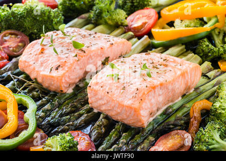Two pieces of fillet of baked salmon on green asparagus, pepper, cherry tomatoes and broccoli on baking tray garnished with fresh thyme. Cooked lunch  Stock Photo