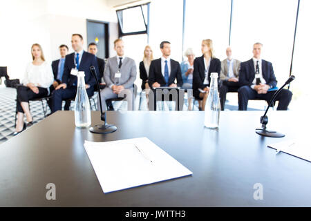 Audience of business people sitting at training room, conference hall, view from speaker table with documents, microphones and water Stock Photo