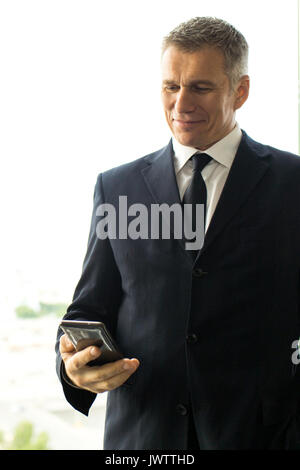 Mature businessman using smartphone standing near office window with view of city Stock Photo