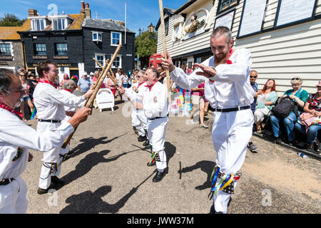 Traditional English folk dancers, Woodchurch Morris group, dancing on seafront harbour jetty during Broadstairs Folk Week. Wearing all white costume, holding poles, dancing in two rows. Stock Photo