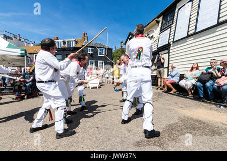 Traditional English folk dancers, Woodchurch Morris group, dancing on seafront harbour jetty during Broadstairs Folk Week. Wearing all white costume, holding poles, dancing in two rows. Stock Photo