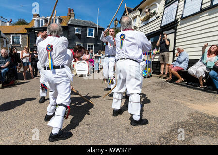 Traditional English folk dancers, Woodchurch Morris group, dancing on seafront harbour jetty during Broadstairs Folk Week. Wearing all white costume, holding poles, dancing in two rows. Stock Photo