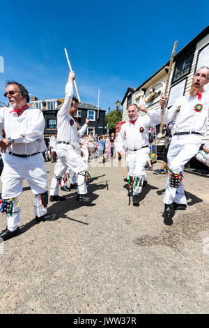 Traditional English folk dancers, Woodchurch Morris group, dancing on seafront harbour jetty during Broadstairs Folk Week. Wearing all white costume, holding poles, dancing in two rows. Stock Photo