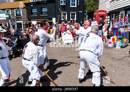 Traditional English folk dancers, Woodchurch Morris group, dancing on seafront harbour jetty during Broadstairs Folk Week. Wearing all white costume, holding poles, dancing in two row. Stock Photo