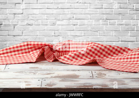Empty wooden table with red checked tablecloth over brick wall background Stock Photo