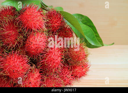 Bunch of Fresh Ripe Rambutan Fruits with Green Leaves on the Wooden Table Stock Photo