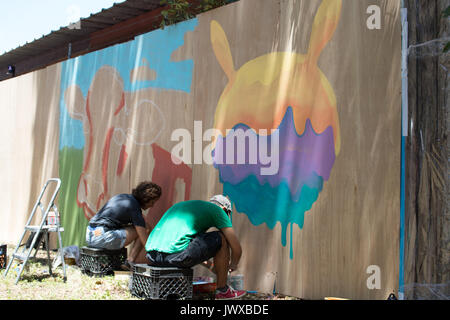 Two artists sitting on crates painting a multicolored mural at Austin Ice Cream Festival. Stock Photo