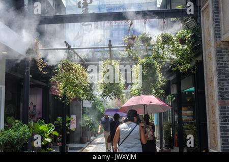 Tourists wander the streets of Tianzifang in Shanghai, China. A cooling system sprays a mist to bring relief from the hot sun. Stock Photo