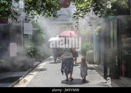 A mother and child walk around the streets of Tianzifang in Shanghai, China. Mist is sprayed from a cooling system to bring relief form the hot sun. Stock Photo