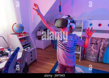 Little boy, 7 years old, plays a 3-D computer game, with a virtual reality headset, in his children's room, Stock Photo