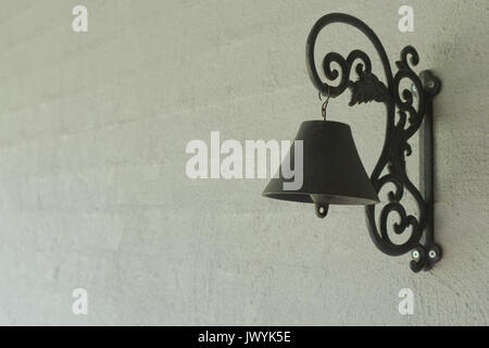 A black iron door bell hanging on a grey rendered brick wall in the entrance way to a home. Stock Photo